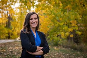 a photo of a woman with her arms cross with fall trees in background