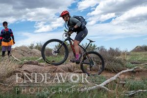 woman mountain biker wheelie over rock step